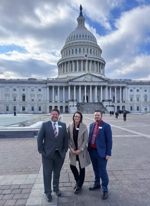 Two men and a woman pose in front of the U.S. Capitol