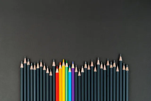 A row of black pencils and handful of rainbow pencils in the center. 