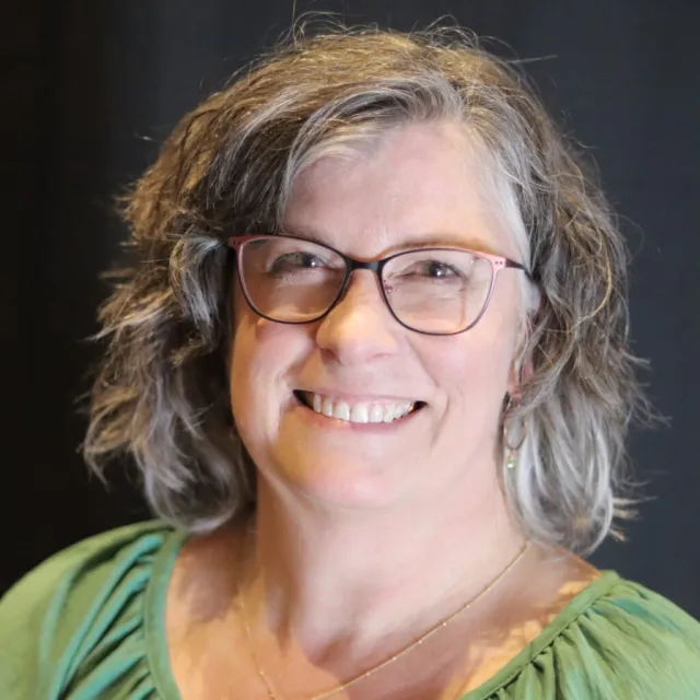 A woman wearing glasses and a green top smiles at the camera