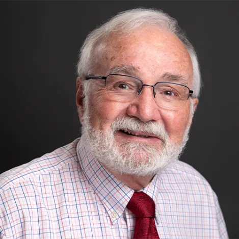 A man with a white beard and glasses wearing a checked shirt and red tie