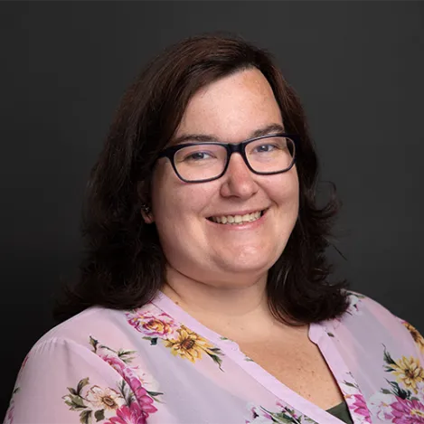 A woman with dark hair and glasses smiles at the camera