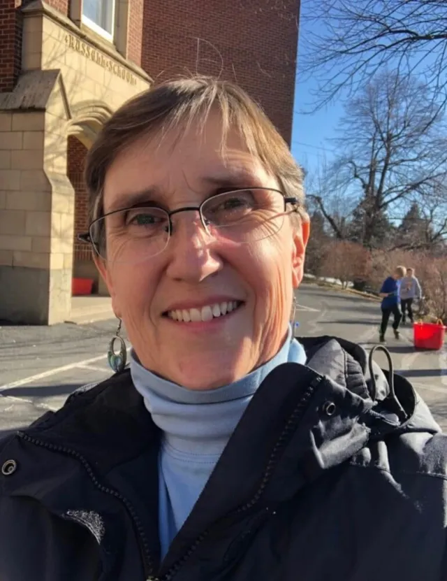 A woman with short hair and glasses smiles at the camera