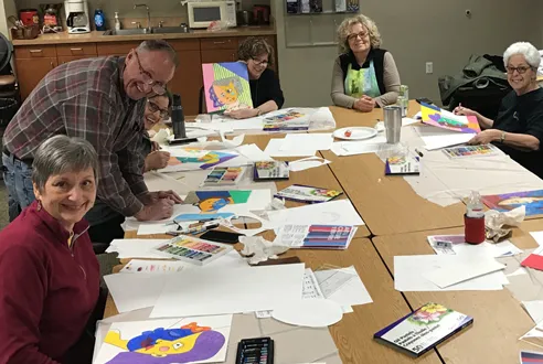 A group of older people create art around a table