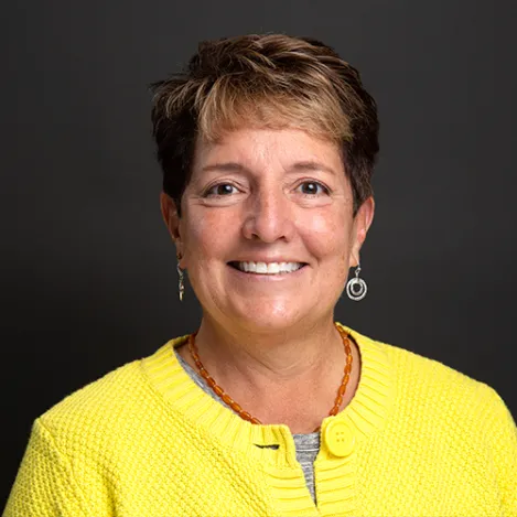 A woman with short hair wearing a yellow shirt smiles at the camera