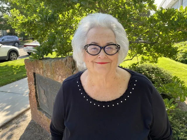 A woman with white hair and dark glasses smiles at the camera