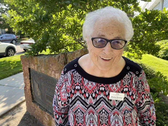 A woman with short white hair and dark glasses smiles at the camera