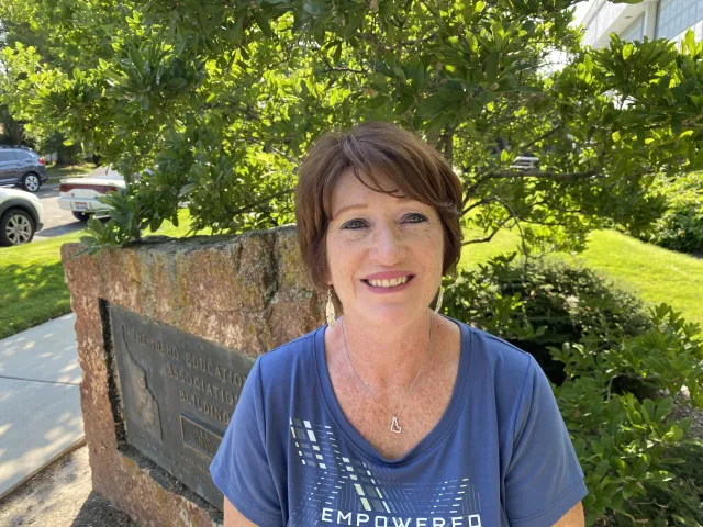 A woman with dark brown hair and a blue shirt smiles at the camera