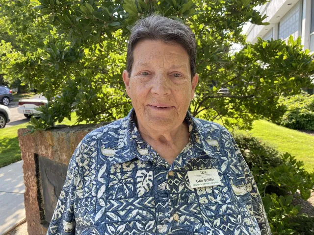 A woman with short gray hair and a blue patterned shirt smiles at the camera