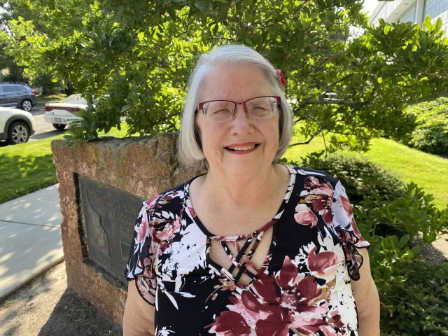 A woman with a white bob and glasses smiles at the camera