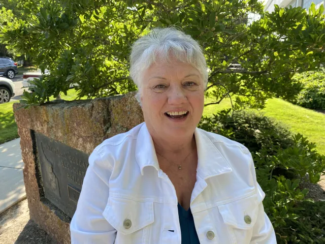 A woman with short white hair and a white denim jacket smiles at the camera