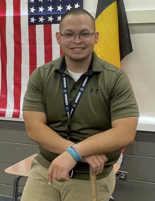 A man in a green shirt and wearing glasses smiles at the camera