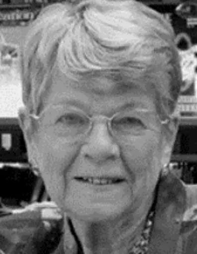 An historic photo of a woman with short hair and glasses smiling at the camera