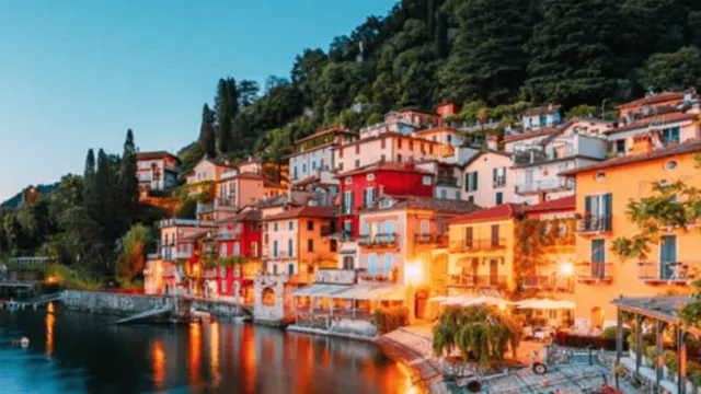 A beautifully lit resort on a lake in a lush wooded area.