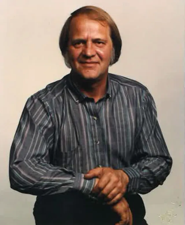 A man in a striped dark shirt smiles at the camera