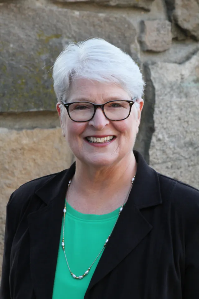 A woman with white hair and black glasses smiles at the camera