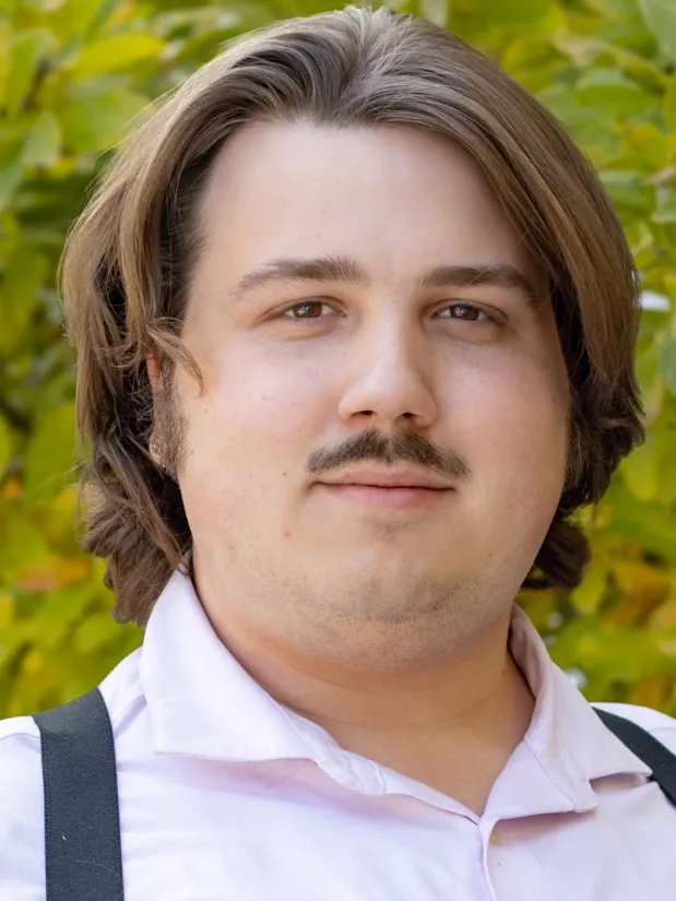 A man with brown hair and a mustache smiles at the camera