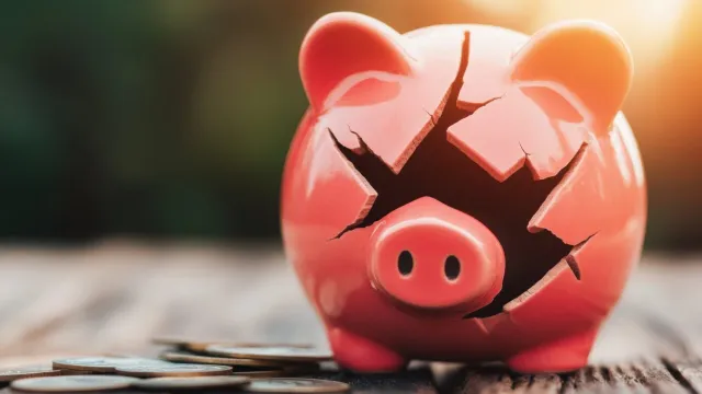 Piggy bank is cracked and broken, money lies around it. 