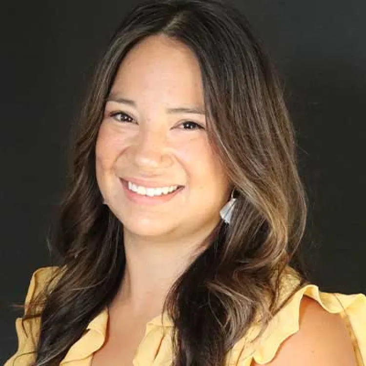 A woman with brown hair and wearing a yellow shirt smiles at the camera