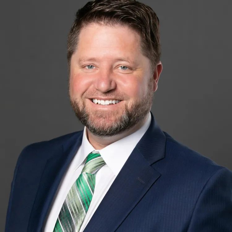 A bearded man wearing a blue blazer, green shirt and white tie