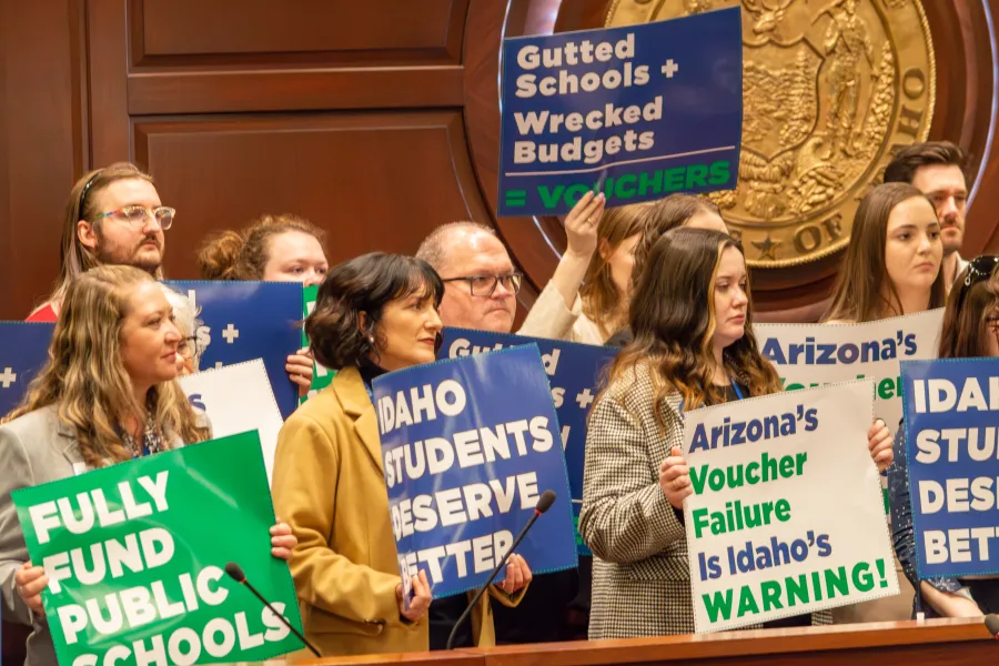 Group holding blue and green signs, listening to a speaker.