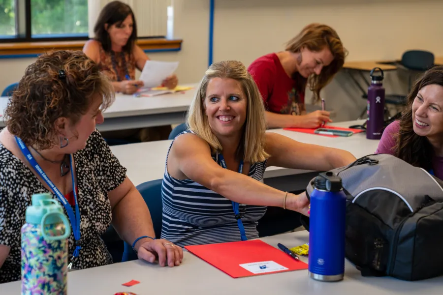 Three women smile and talk while seated at a table. 